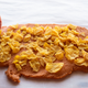 Photo of cornflakes laid out on the peanut butter and candy corn mixture. They're shingled in one layer.